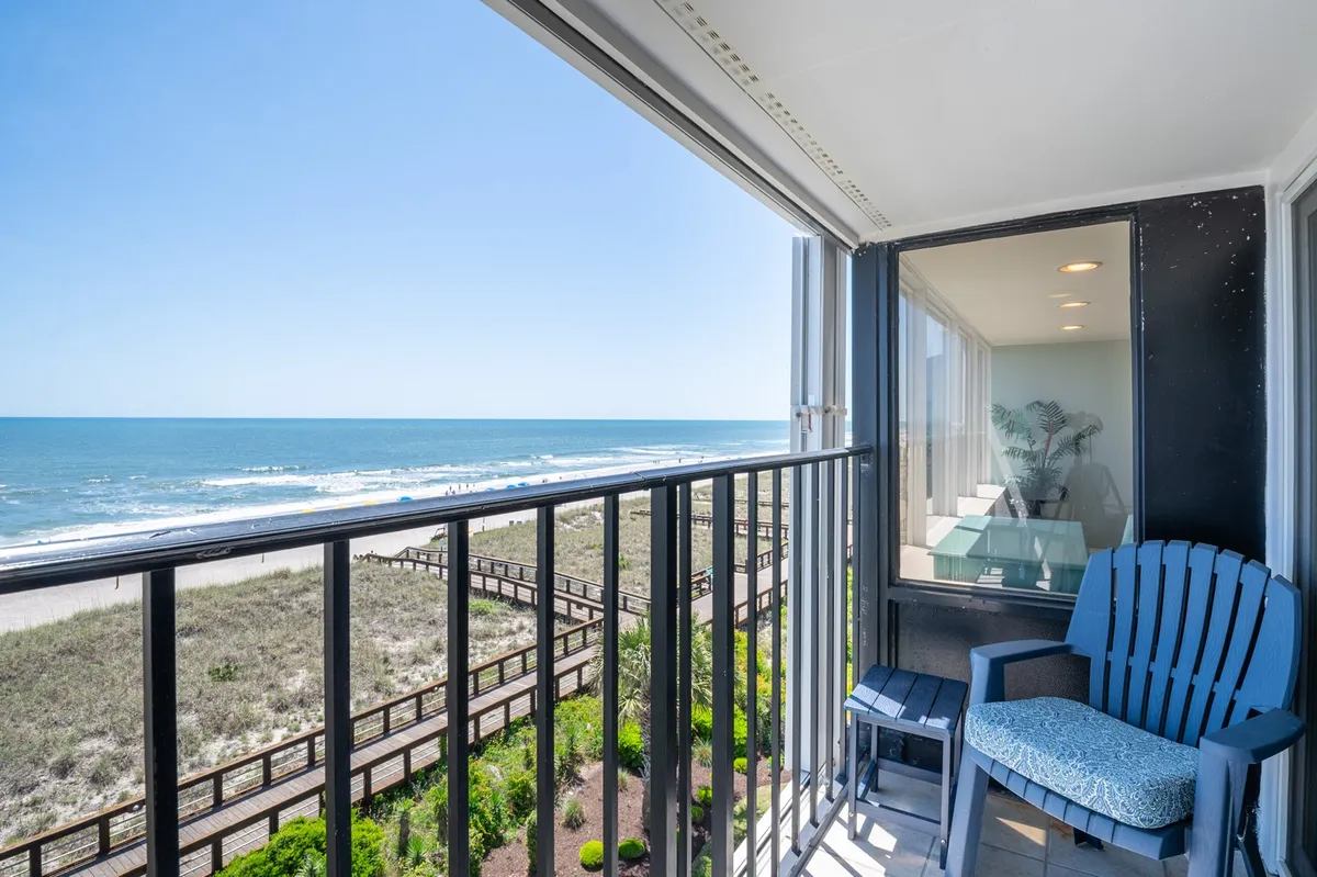 A tranquil balcony scene overlooking the ocean and landscaped gardens, with comfortable chairs perfectly positioned for enjoying the view. The scene suggests a peaceful place to watch fireworks or unwind after a day of exploration.