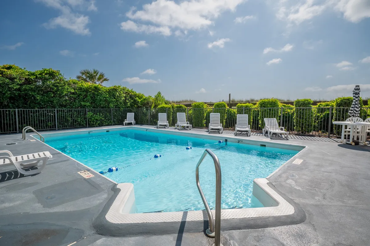 This image features the property’s inviting swimming pool surrounded by lounge chairs and lush greenery. The scene suggests a space perfect for group relaxation, swimming, and sunbathing after a day or evening out exploring the boardwalk.