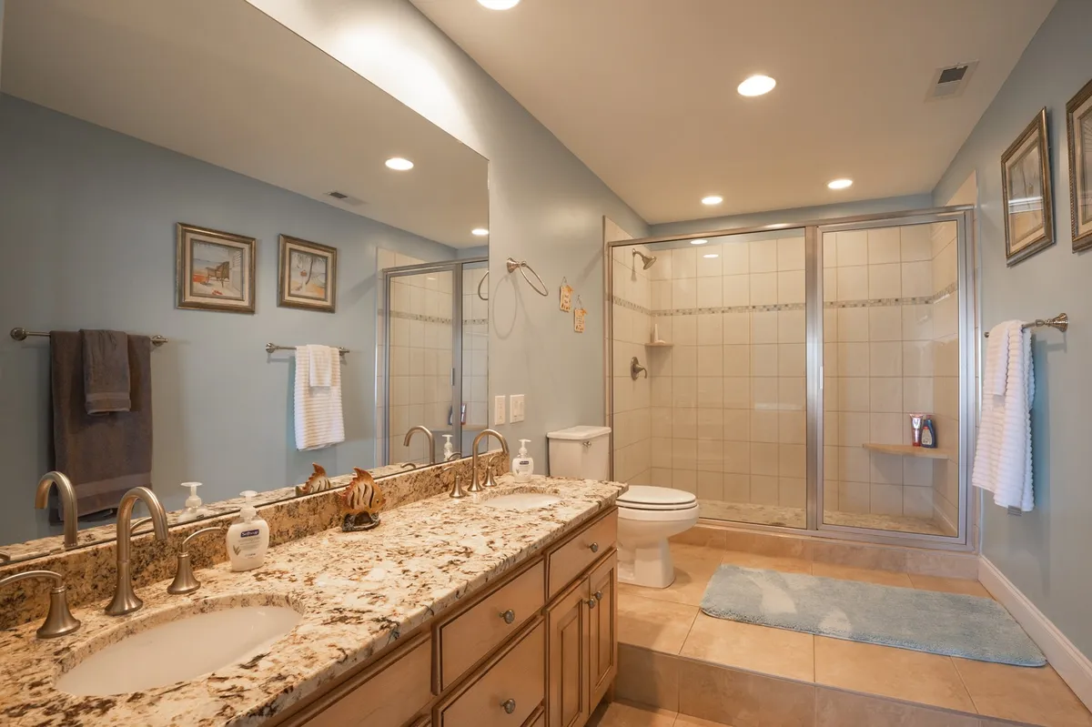 A modern bathroom with granite countertops, double sinks, large mirrors, and a walk-in shower. The calm, spa-like atmosphere encourages relaxation after busy beach days.