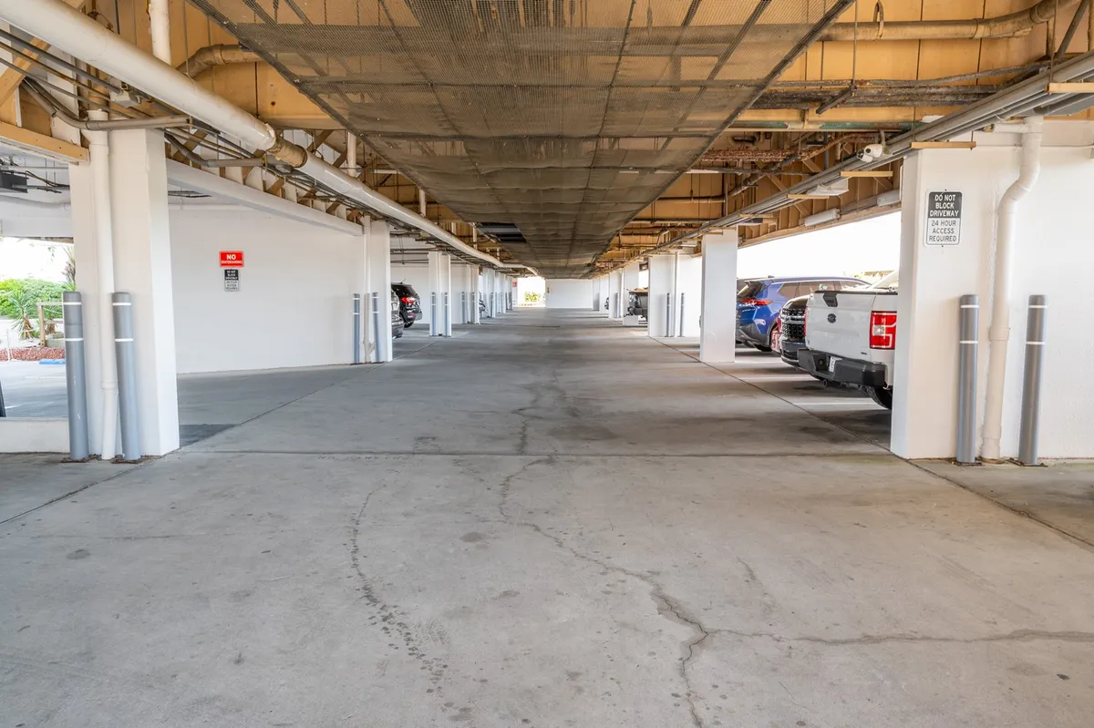 The parking area beneath the building features clearly marked spaces and sturdy structural columns, offering a direct view of the protected, gated environment. The scene is functional but reassuring, emphasizing security and convenience.