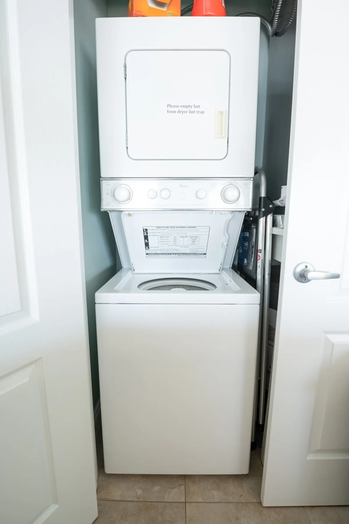 This image focuses on a stacked washer-dryer unit, neatly tucked into a practical, easily accessible area. Safety items and clear instructions show a well-organized space dedicated to household chores.