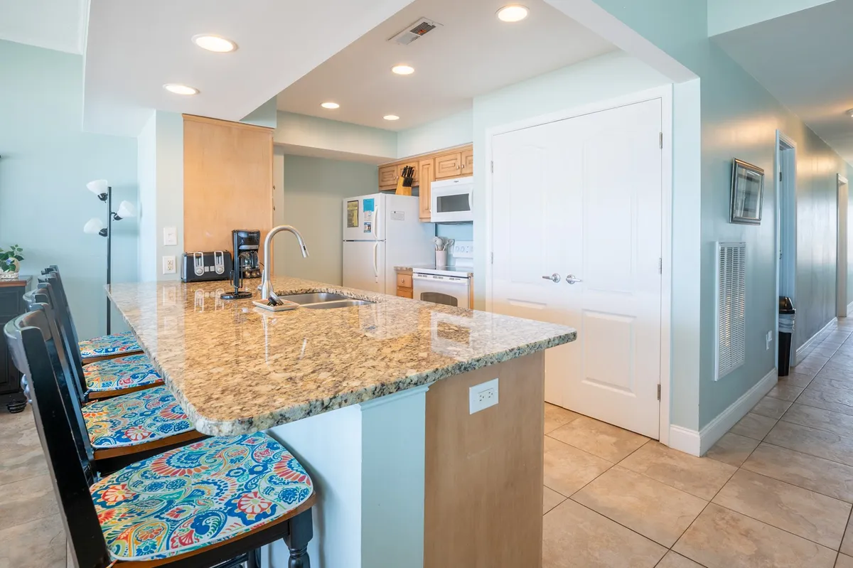 This image captures a bright, inviting kitchen featuring a granite countertop, colorful bar stools, and modern appliances. The space radiates a cheerful atmosphere perfect for meal preparation and casual dining, reflecting the kitchen as a social hub within the home.
