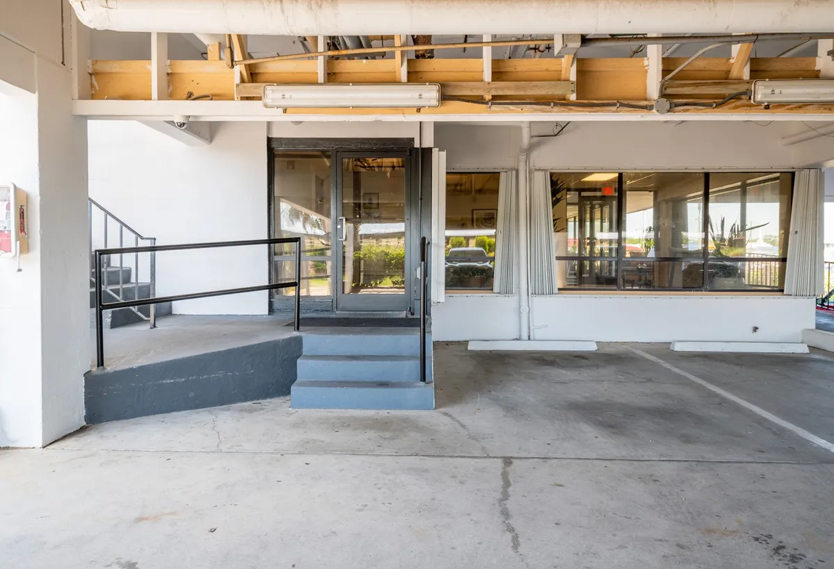 The image shows the stylish entrance steps leading up to the property with inviting glass doors and an exposed ceiling above, blending a sense of arrival with anticipation for social experiences.