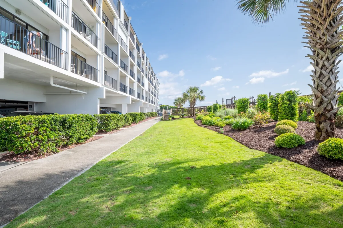 A lush green lawn leads to a palm tree and a walkway heading toward a playground, with balconies of the building visible. The scene radiates a cheerful, relaxed mood, ideal for family strolls, outdoor gatherings, and playtime.